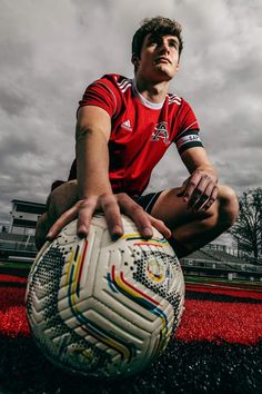 a young man sitting on the ground holding a soccer ball