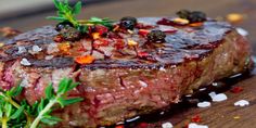 a piece of steak on a wooden cutting board with garnish and seasoning