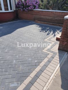 a brick driveway with the word luxury written on it in front of a house and purple flowers