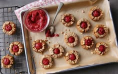 raspberry cookies on a baking sheet with a bowl of jam