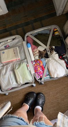 a person standing in front of an open suitcase filled with clothing and other items on the floor