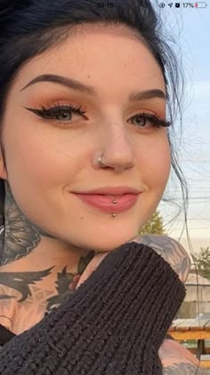 a close up of a person with tattoos on her face and arm, wearing a sweater