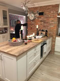 a woman is standing in the middle of a kitchen with white cabinets and wooden counter tops