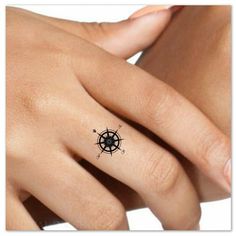 a woman's hand with a small black compass tattoo on her left ring finger