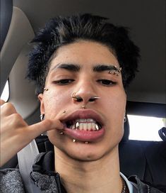 a young man with piercings on his nose is sitting in the back seat of a car