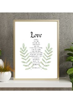 a framed print with the words love in black and white on it next to potted plants