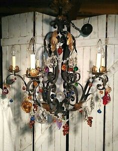 a chandelier hanging from the ceiling in front of a white wooden wall with glass beads