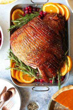 a roasted ham with oranges and cranberries on a platter next to silverware