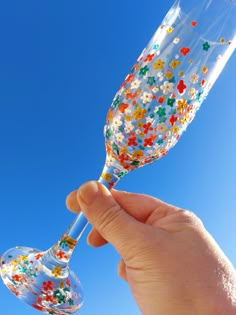 a hand holding a wine glass with colorful sprinkles on the outside and inside