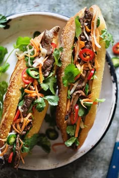 two sub sandwiches on a plate with lettuce, carrots and other toppings