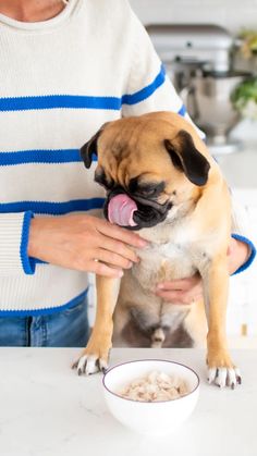 a person holding a small dog in their lap while eating food from a white bowl