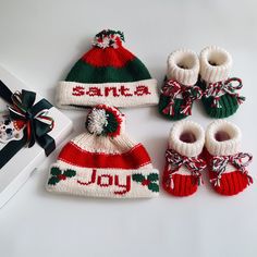 knitted christmas hats, mittens and booties are sitting next to a gift box