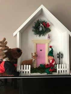 a christmas scene with elf and reindeer in front of a pink door on a shelf