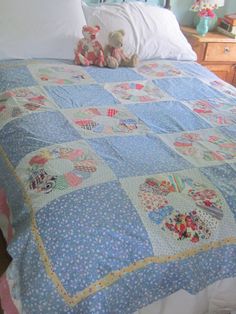 a teddy bear sitting on top of a blue quilted bedspread with white pillows