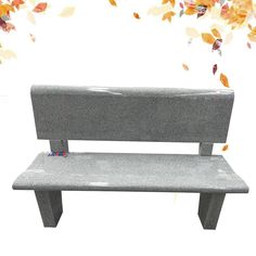 a gray bench sitting in front of a tree with leaves falling from the branches behind it