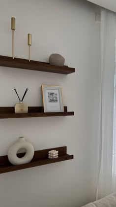 two shelves with candles and pictures on them in a room next to a window that has sheer curtains