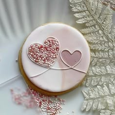 a cookie decorated with two hearts sitting on top of a plate next to some sprinkles