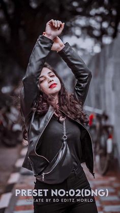 a woman in black leather jacket and pants posing for the camera with her arms up