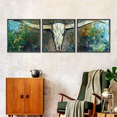 three paintings hang on the wall next to a green chair and wooden cabinet with a vase in it