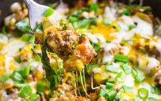 a spoon full of food that is being lifted from a skillet with vegetables and meat