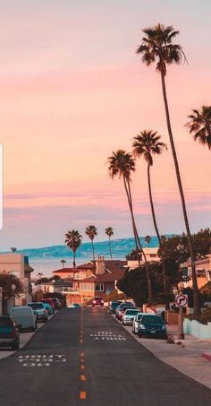 a street with cars parked on the side and palm trees in the background at sunset