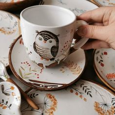 a person holding a coffee cup and saucer in front of plates with owls on them