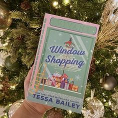 someone holding up a book in front of a christmas tree