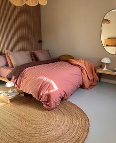 a bed with pink sheets and pillows in a bedroom next to a round rug on the floor