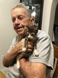 an older man holding a kitten in his arms