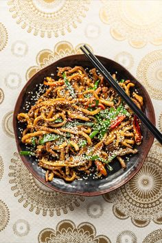 a bowl filled with noodles and vegetables next to chopsticks on top of a table