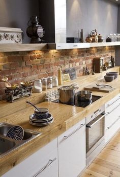 a kitchen with white cabinets and wooden counter tops, along with a brick wall in the background