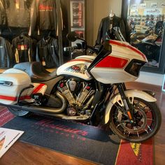 a white and red motorcycle parked in front of a display case with black leather jackets on the wall