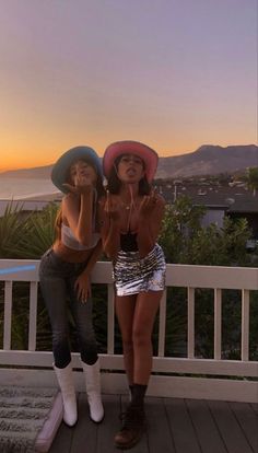 two women standing on a porch with their hands up in the air and one is wearing a cowboy hat