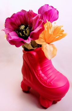 a red vase with flowers in it on a white table next to a pink boot