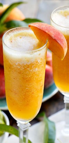 two glasses filled with orange juice and topped with sliced peaches next to some apples