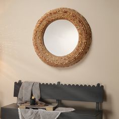 a round mirror hanging on the wall above a bench with a blanket and candle next to it