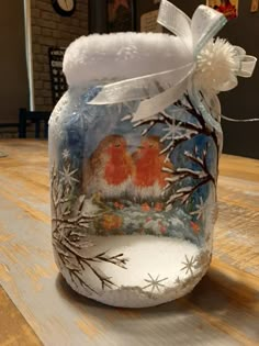 a glass jar decorated with two birds and snowflakes on the inside, sitting on a wooden table