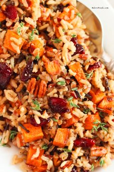 a white plate topped with rice, cranberries and carrots next to a fork