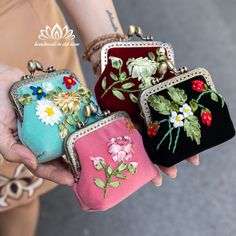 three small purses with flowers on them are held in the palm of a woman's hand