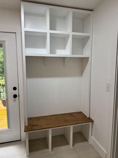 an empty room with white shelving and wooden bench in the corner, next to a glass door