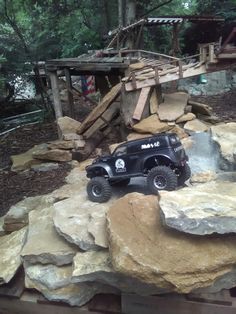 a toy truck is parked on top of some rocks in the woods near a bridge