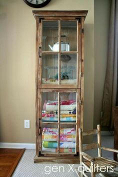 a wooden cabinet filled with lots of different colored fabrics in front of a wall clock