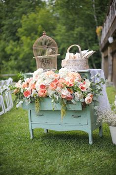 a table with flowers and birdcage on it in the middle of a field