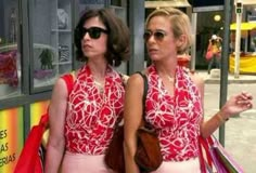 two women are walking down the street with shopping bags in hand and one is wearing sunglasses