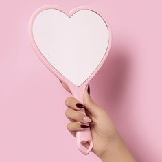 a hand holding a pink heart shaped mirror