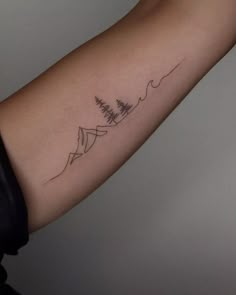 a woman's arm with a tattoo on it that has trees and mountains in the background