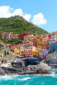 the colorful village is perched on top of a hill above the blue water and rocks