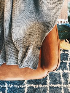 a chair with a blanket on top of it next to a plant and potted plants