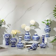 several blue and white vases with flowers in them on a table next to a laptop