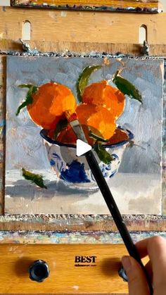 someone is painting oranges in a blue and white bowl on an easel with a brush